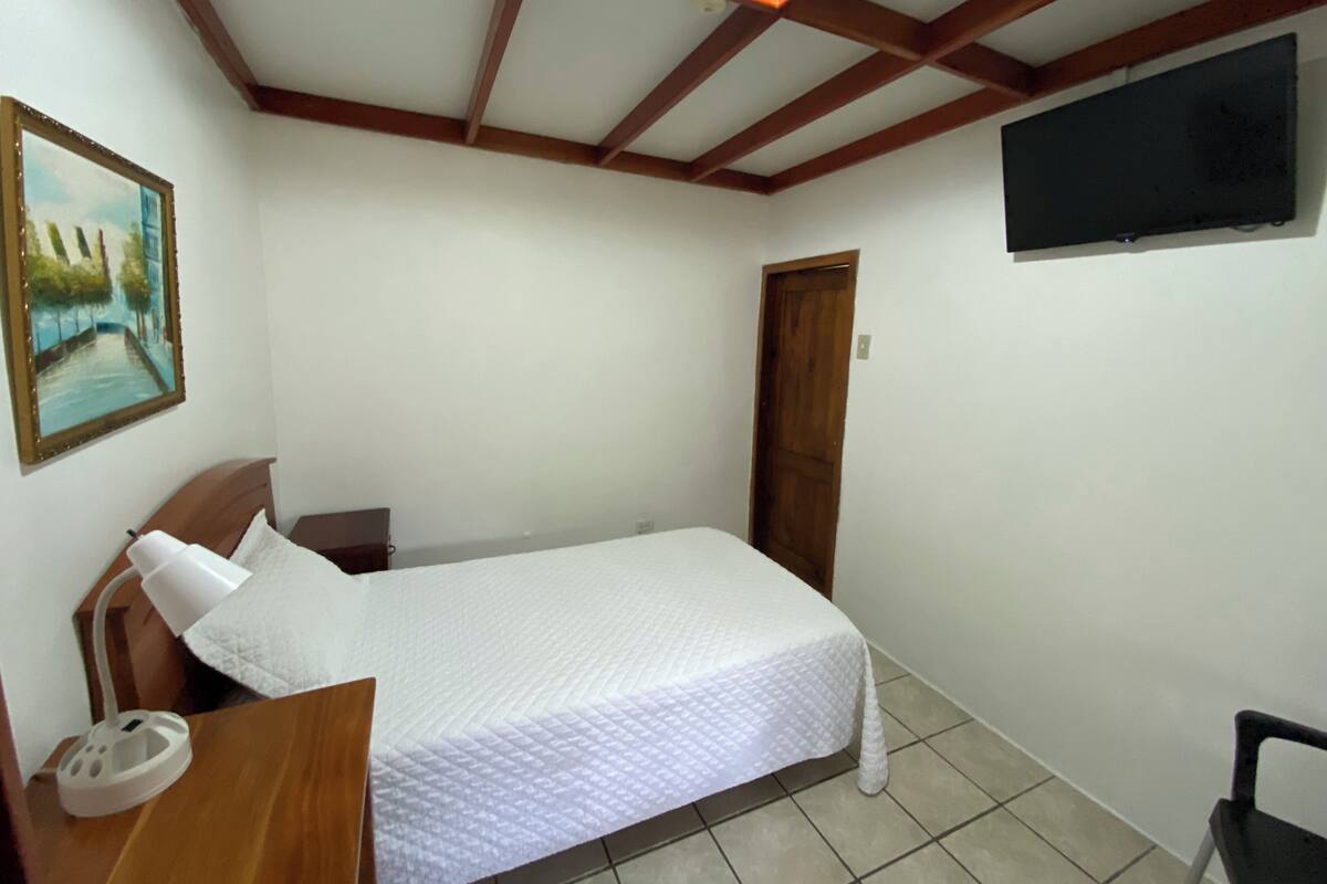 Een slaapkamer met een bed, een bureau, een stoel, een televisie en een schilderij aan de muur.