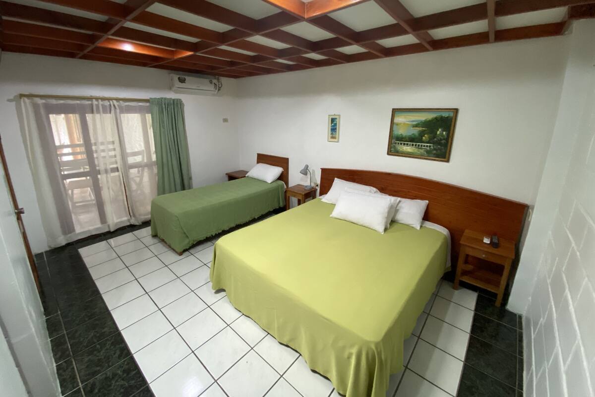Een hotelkamer met twee bedden, een houten plafond, een schilderij aan de muur en een raam met gordijnen.