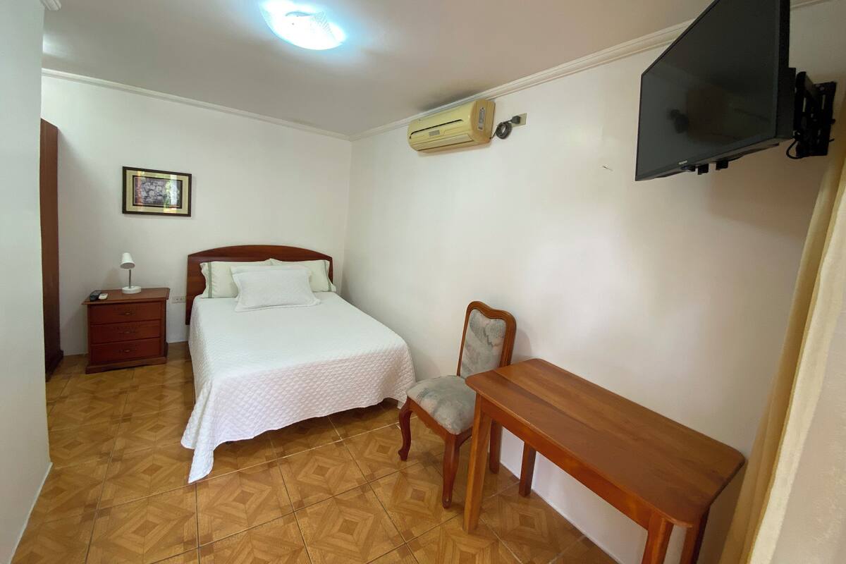Een slaapkamer met een bed, nachtkastje, stoel, televisie en airconditioning.
