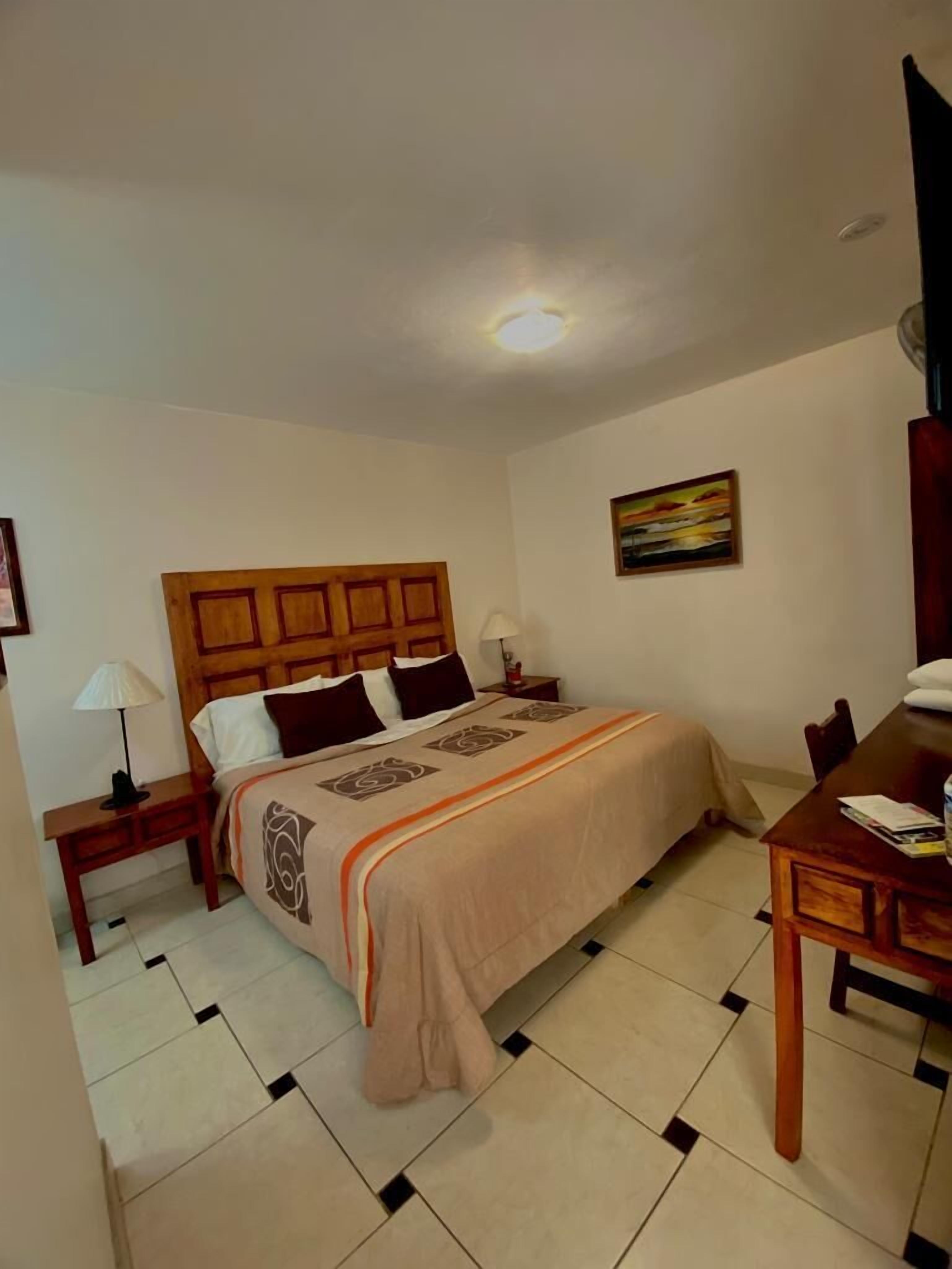 A hotel room with a bed, bedside tables, a desk, and a chair.