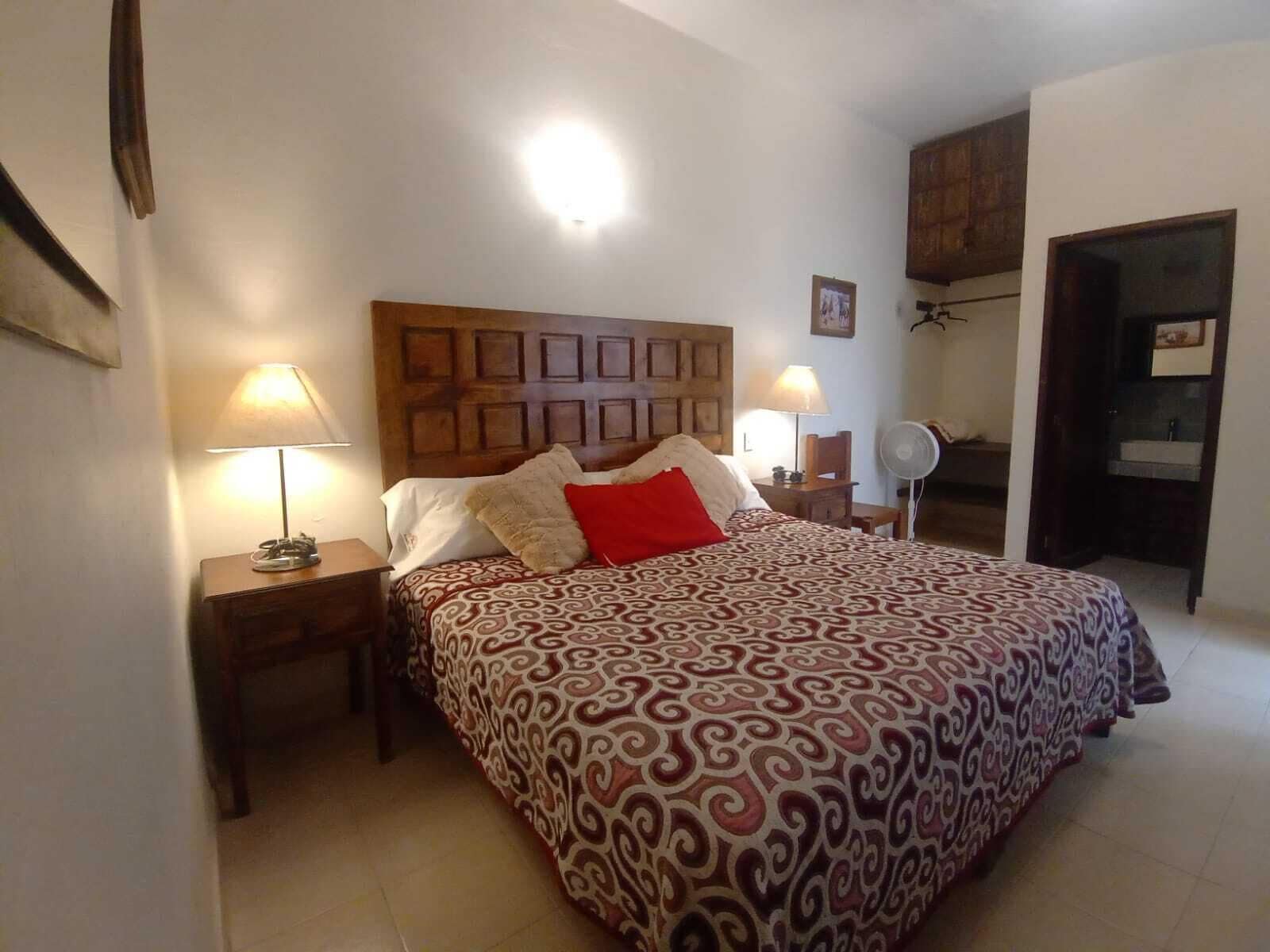 Un dormitorio con colcha estampada, dos lámparas de noche, cabecera de madera y una mesita de noche.