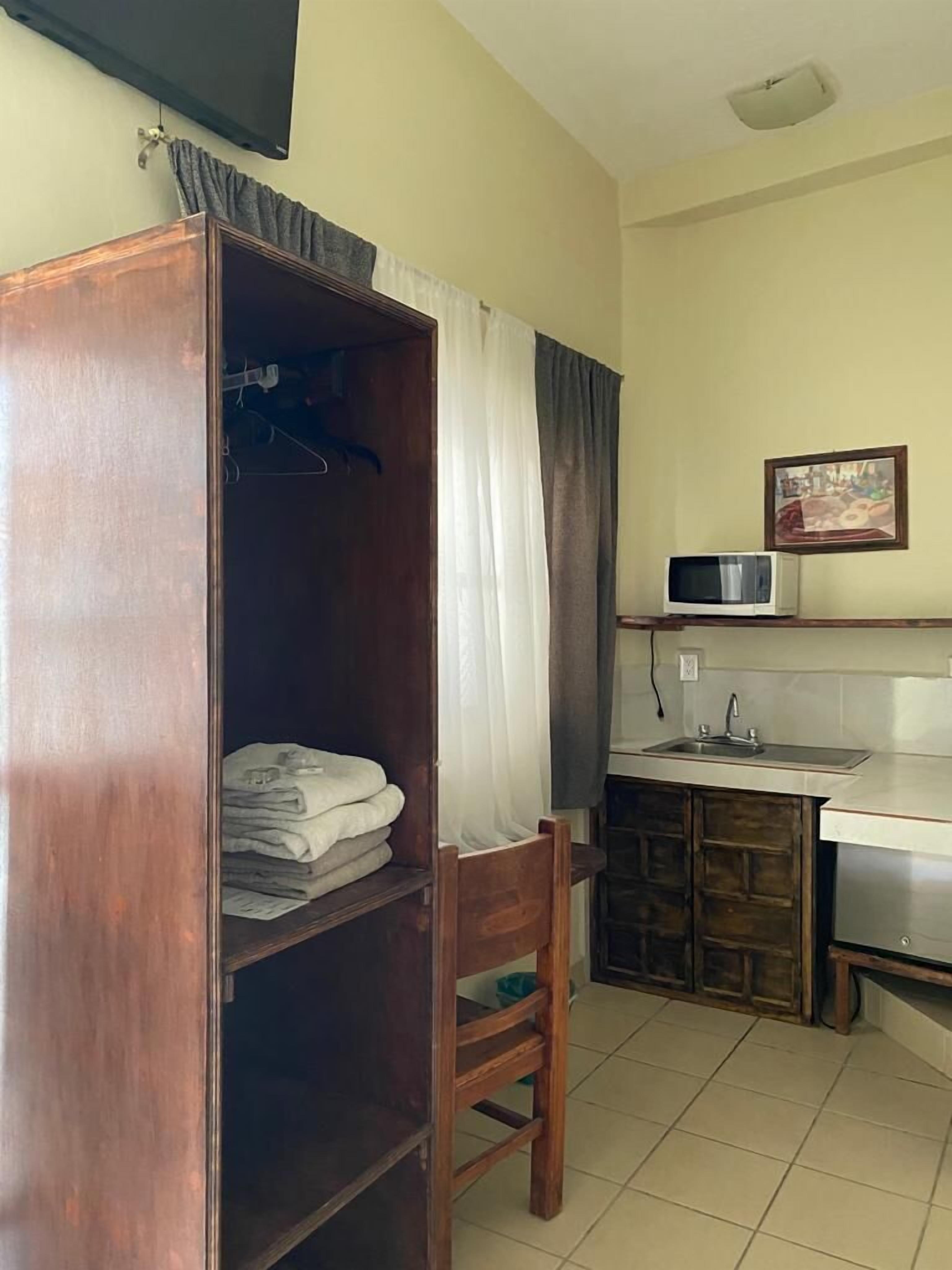 Quarto compacto com guarda-roupa de madeira, uma cadeira, pia e micro-ondas.