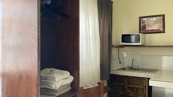 Quarto compacto com guarda-roupa de madeira, uma cadeira, pia e micro-ondas.