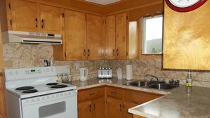 A kitchen with wooden cabinets, a white stove, a sink, and a window. - Gullivers Cove Oceanview Cottages (Gullivers Cove)