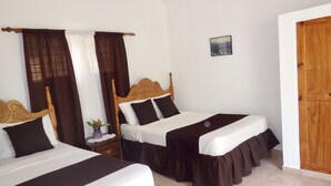 Habitación de hotel con dos camas, cada una con cabecero de madera, ropa de cama blanca y faldas marrones. Hay una mesita con un florero y un cuadro en la pared.