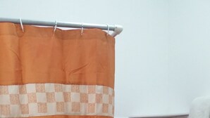Un baño con cortina de ducha naranja, un inodoro blanco y una toalla blanca colgada en la pared.