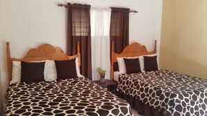 Two single beds with giraffe-patterned bedding, wooden headboards, and a small table with a vase between them.