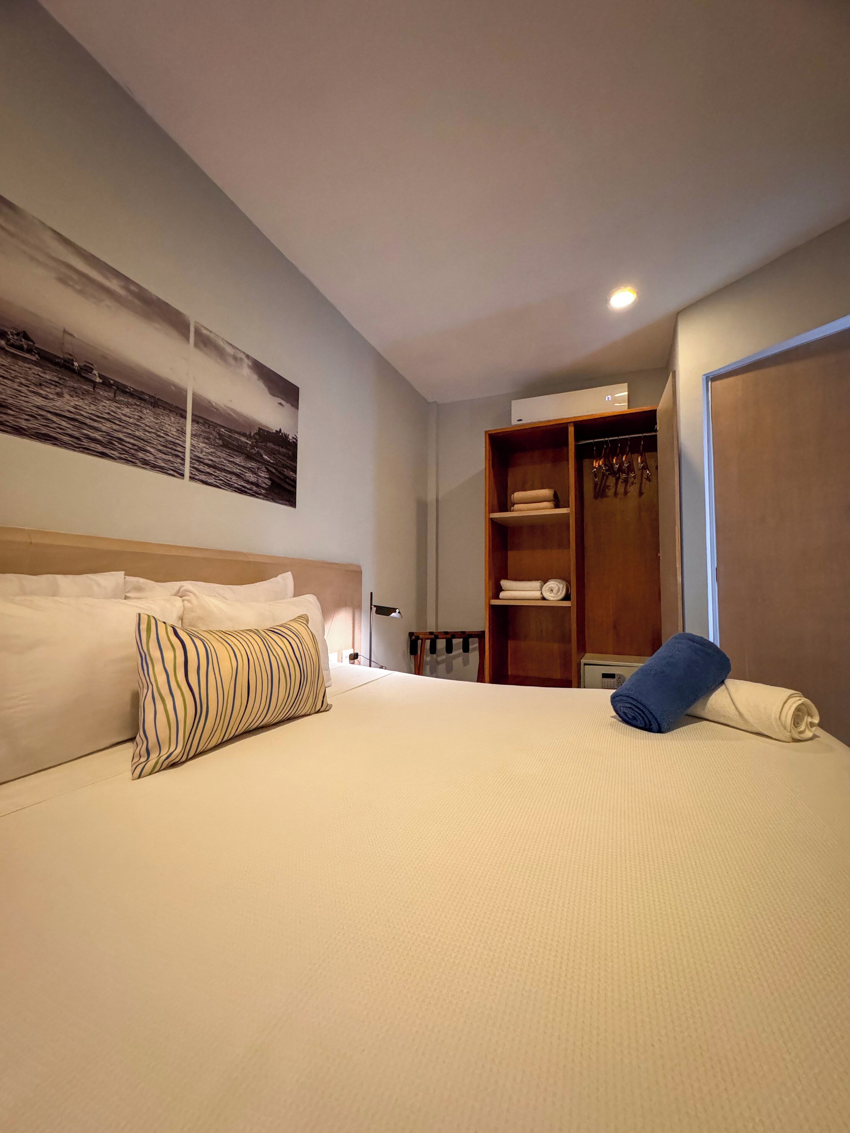 Una habitación de hotel con una cama grande, un armario y un estante en la pared con toallas.