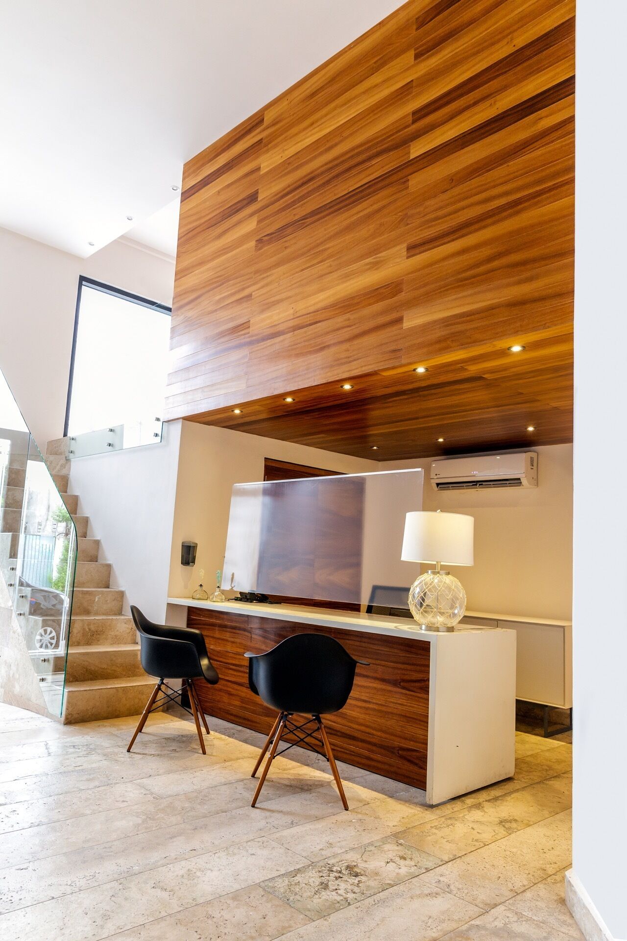 A modern interior with a wooden accent wall, a desk with two chairs, a television, and an air conditioning unit.