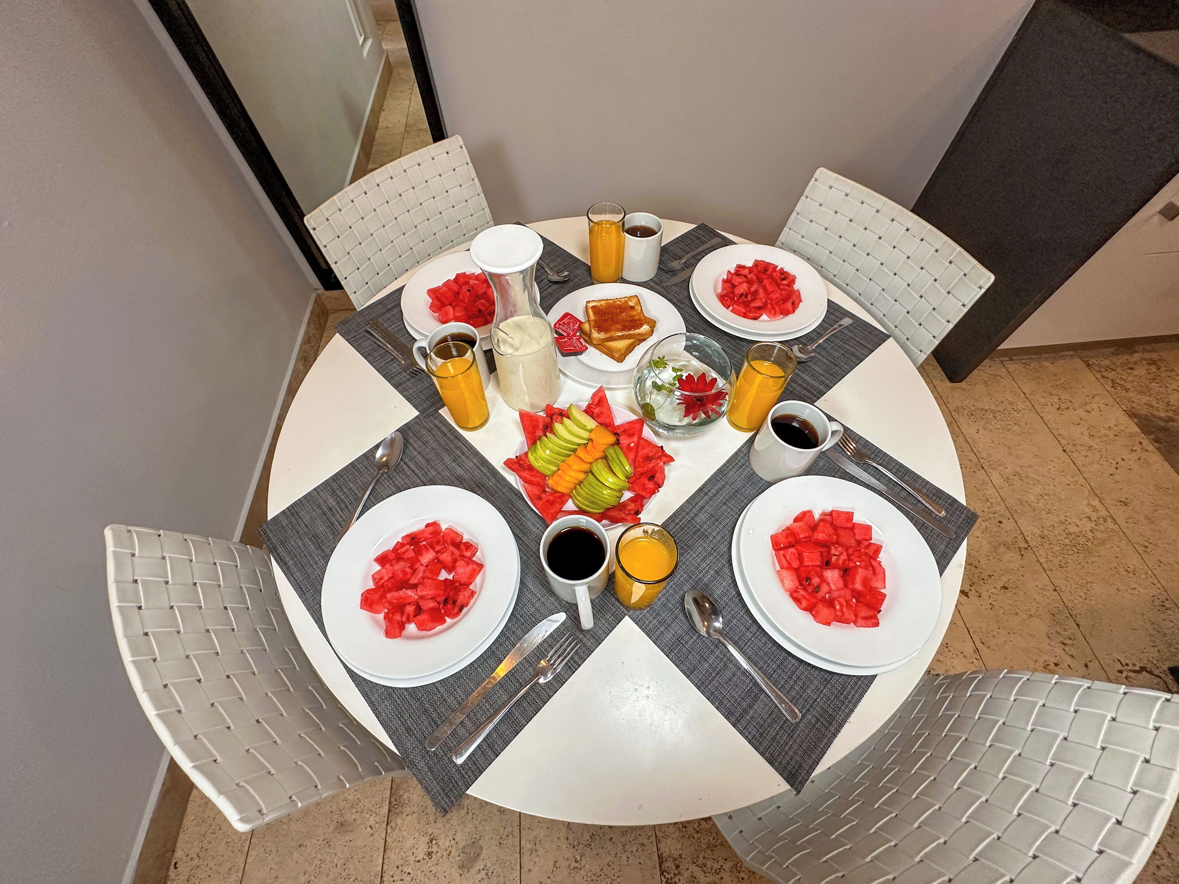 Un tavolo da pranzo rotondo con piatti di anguria e altra frutta, insieme a bicchieri e posate.