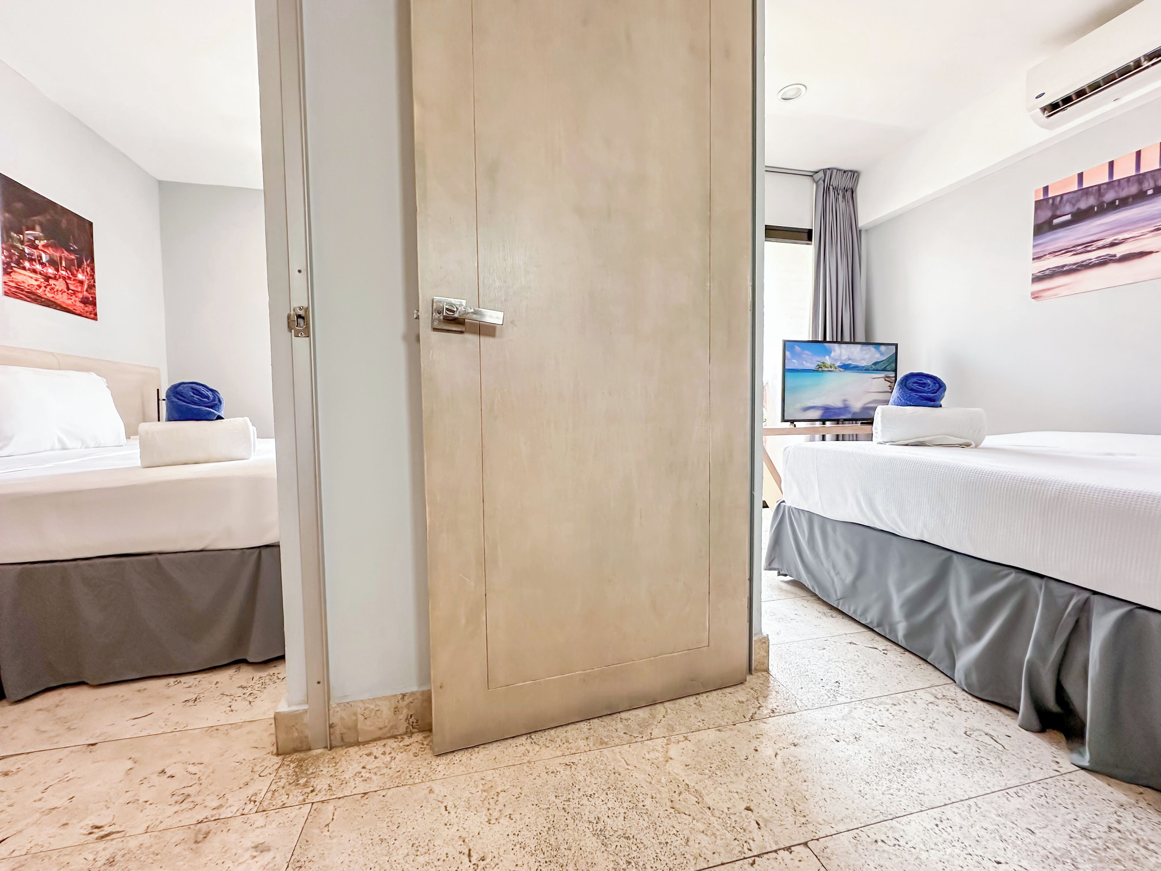 A hotel room with two beds, a large window, a flat-screen TV, and a painting on the wall.