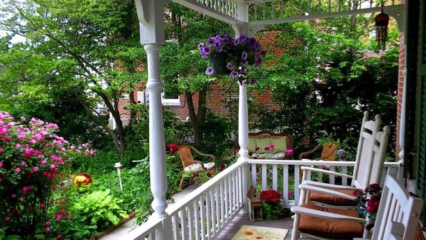 A covered porch with white railings, a hanging flower basket, and a bench with cushions. - Historic Iron Horse Inn (Hermann)