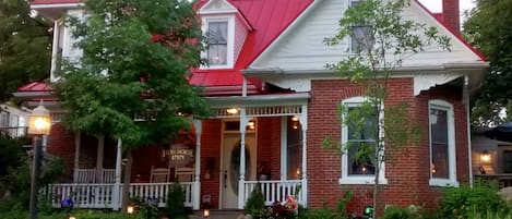 A two-story brick house with a red roof and a porch.