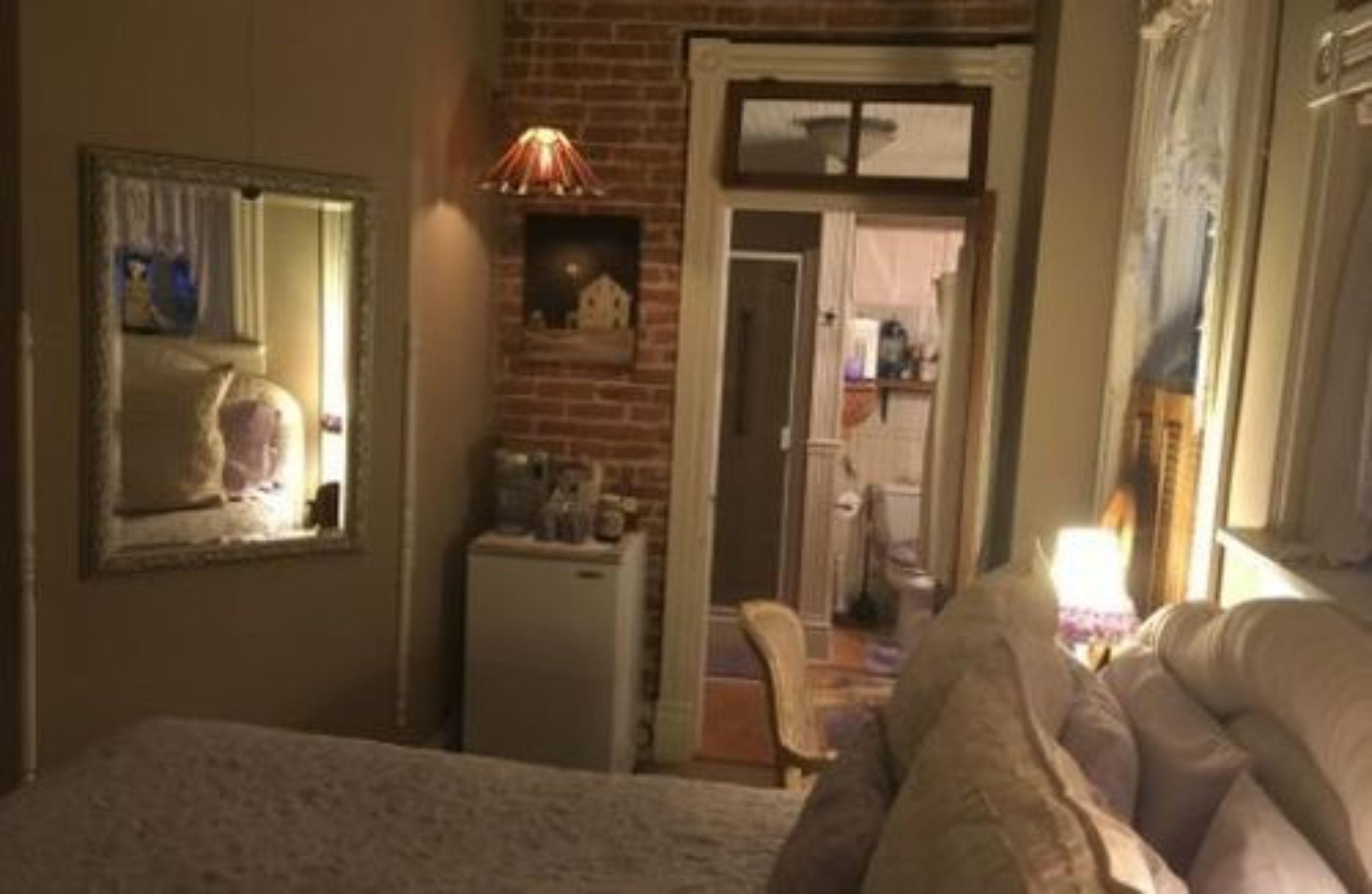 A bedroom with a bed, a dresser, a mirror, a lamp, and a brick wall.