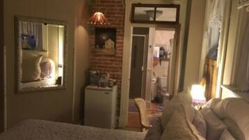 A bedroom with a bed, a dresser, a mirror, a lamp, and a brick wall.