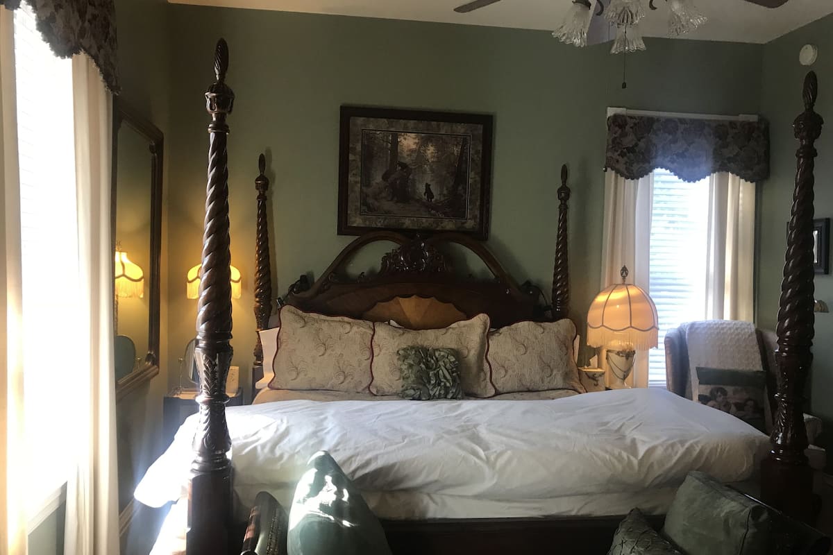 A four-poster bed with a headboard, multiple pillows, and a bedside table with a lamp.