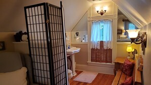 A compact living space with a sofa, a wooden bench, a small table, a window with curtains, a sink, and a lamp. - Historic Iron Horse Inn (Hermann)