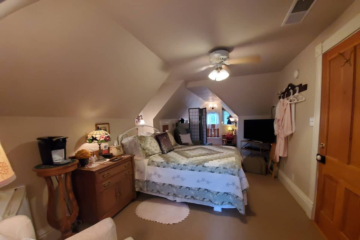 A cozy attic bedroom with a bed, dresser, and a ceiling fan.