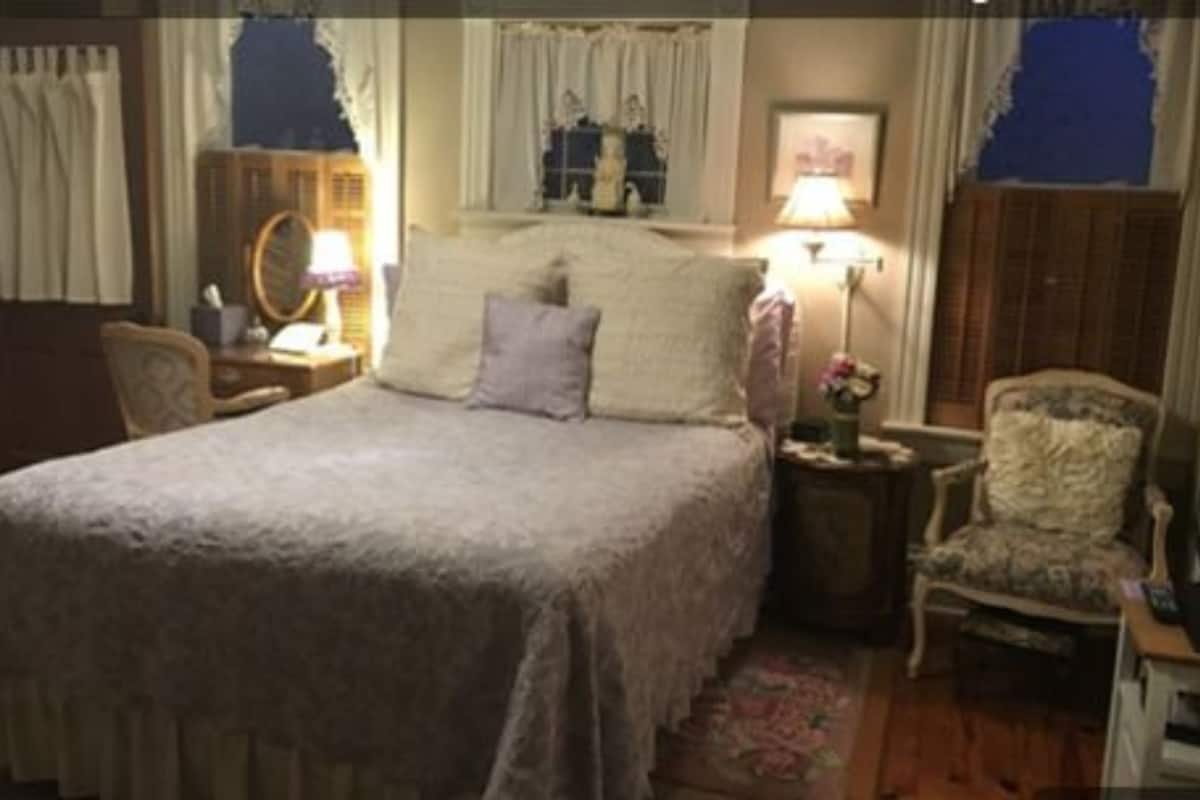 A bedroom with a large bed, a chair, a nightstand, and a lamp.