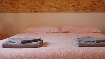 Una cama bien hecha con ropa de cama rosa estampada, dos almohadas y toallas dobladas a cada lado.