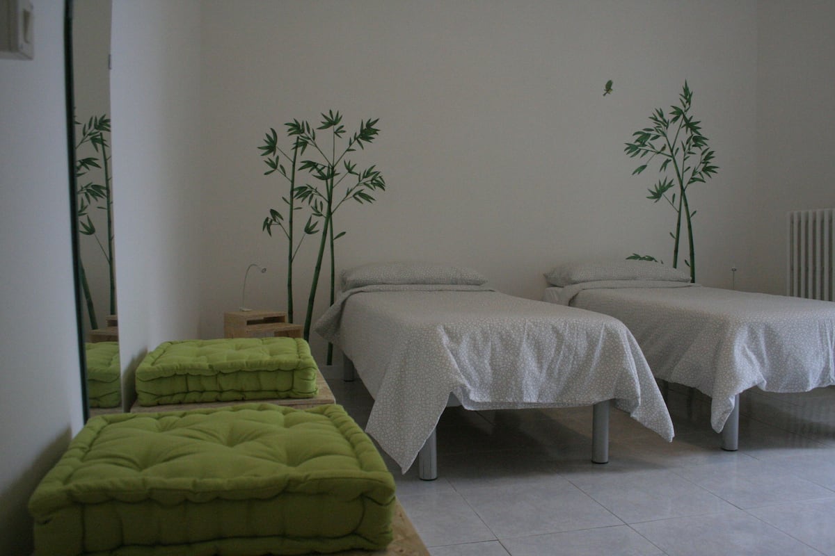 Una habitación con dos camas, un otomano verde y decoración de bambú en las paredes.