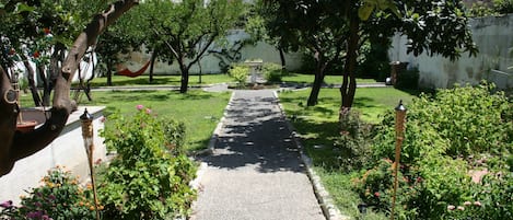 Un sentier bordé de plantes et d’arbres en fleurs, qui mène à un jardin central agrémenté d’une fontaine.