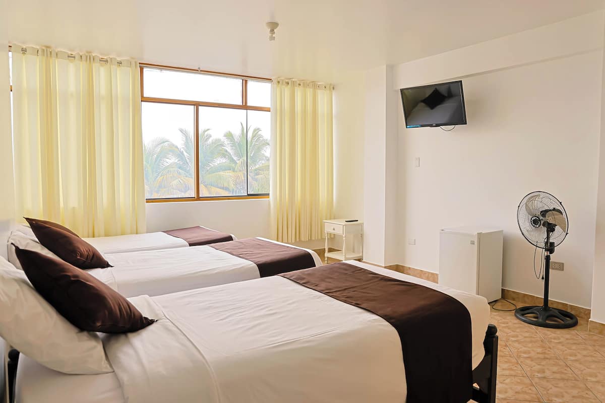 A hotel room with two beds, a TV, a desk, a fan, and a window with curtains.