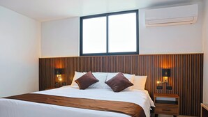 Hotellihuone, jossa on suuri sänky, yöpöytä, seinälle asennettu ilmastointilaite ja ikkuna, jossa on sälekaihtimet.