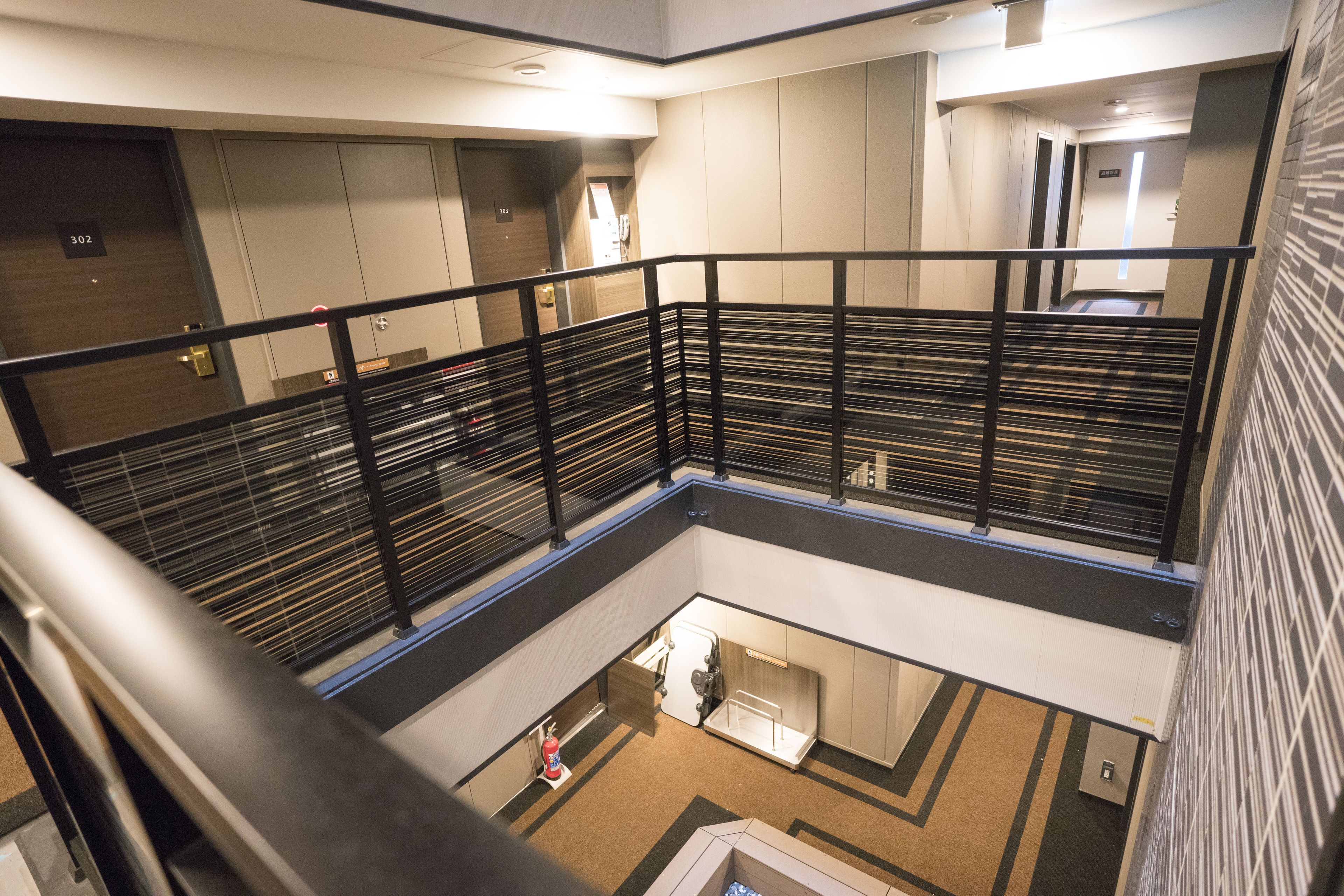 A hotel interior with a modern design, featuring a central atrium, a staircase, and a fire extinguisher near the entrance.