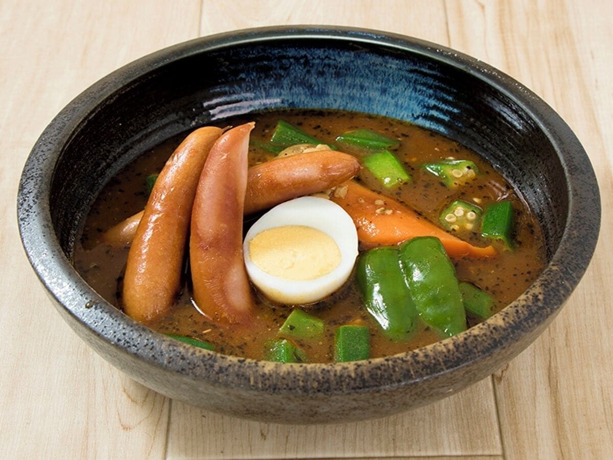 A bowl of soup with sausages, a boiled egg, and green vegetables.