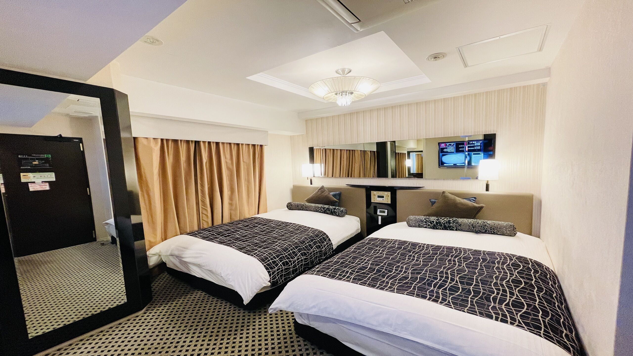 Een hotelkamer met twee bedden, een grote spiegel, een televisie en een plafondlamp.