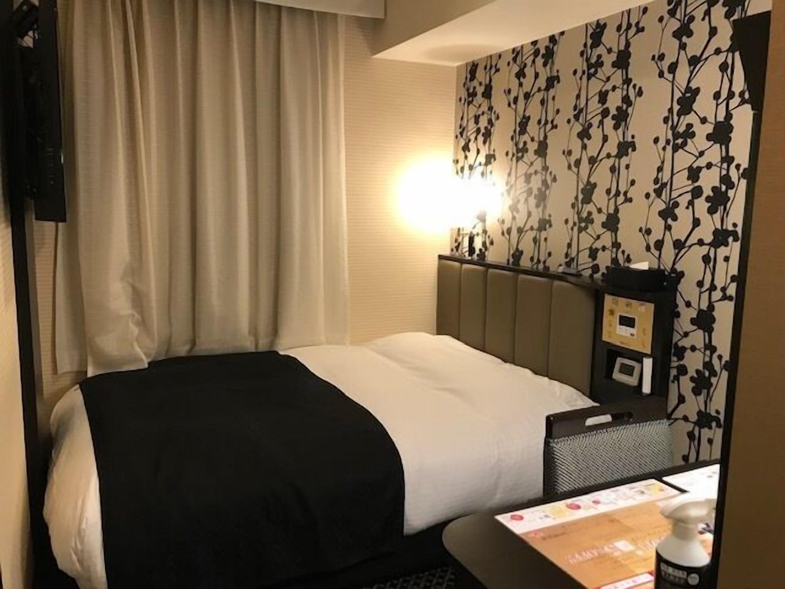 Een hotelkamer met een bed, een bureau met een stoel, een spiegel en een bedieningspaneel aan de muur.