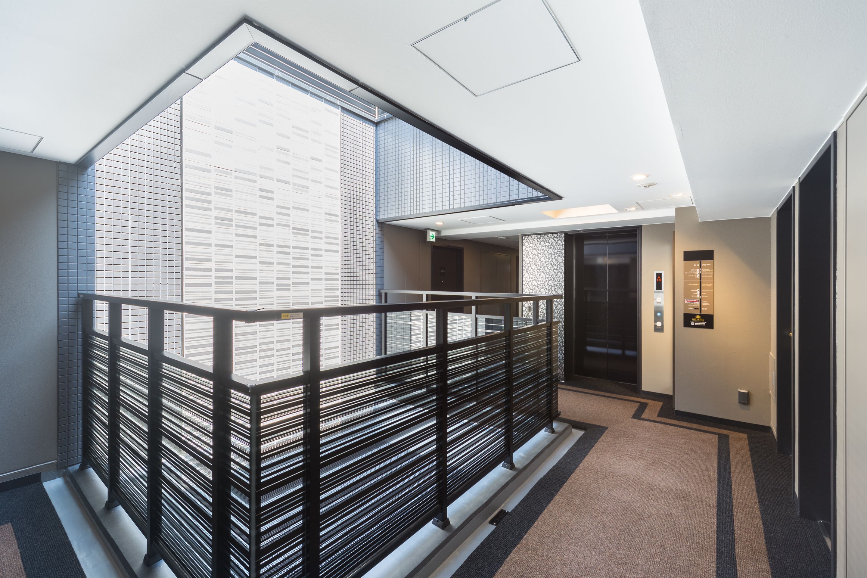 Un intérieur d’hôtel moderne avec un balcon en verre, un escalier et un espace d’accueil.