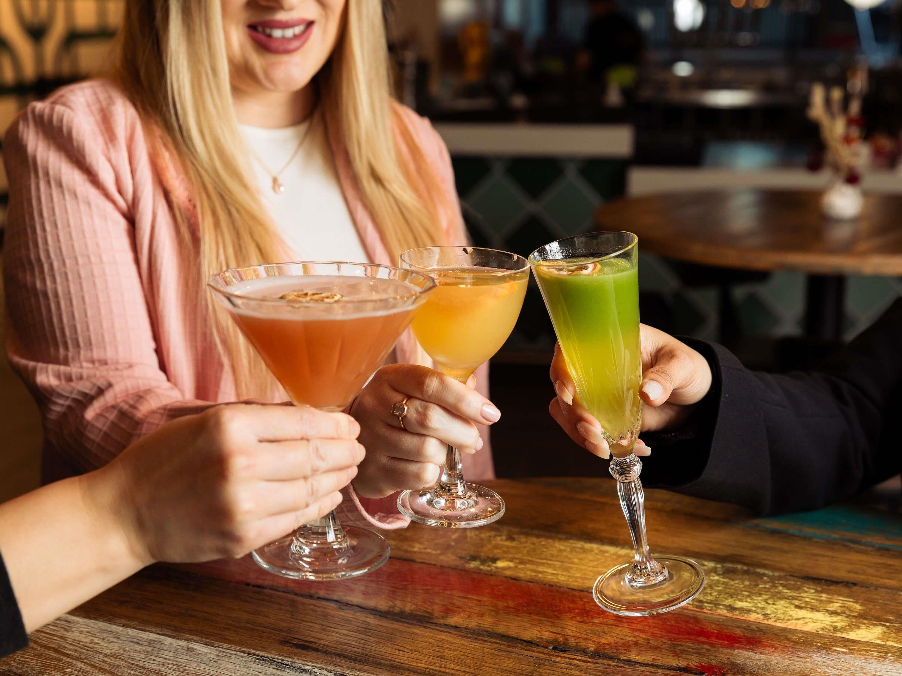 A person holding a martini glass and a highball glass with a green drink.