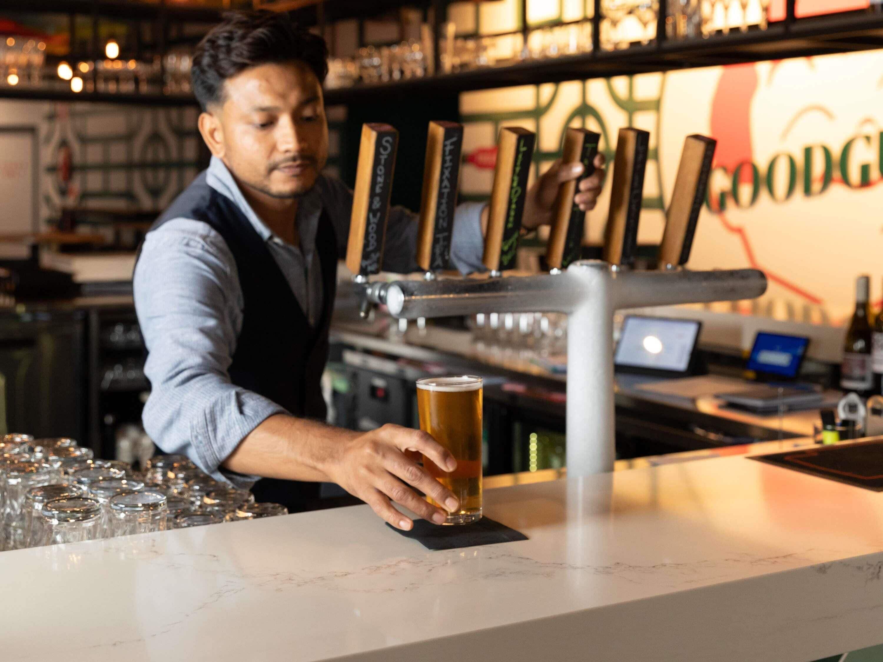 A bartender pouring beer into a glass at a bar with a visible Good Google sign in the background.
