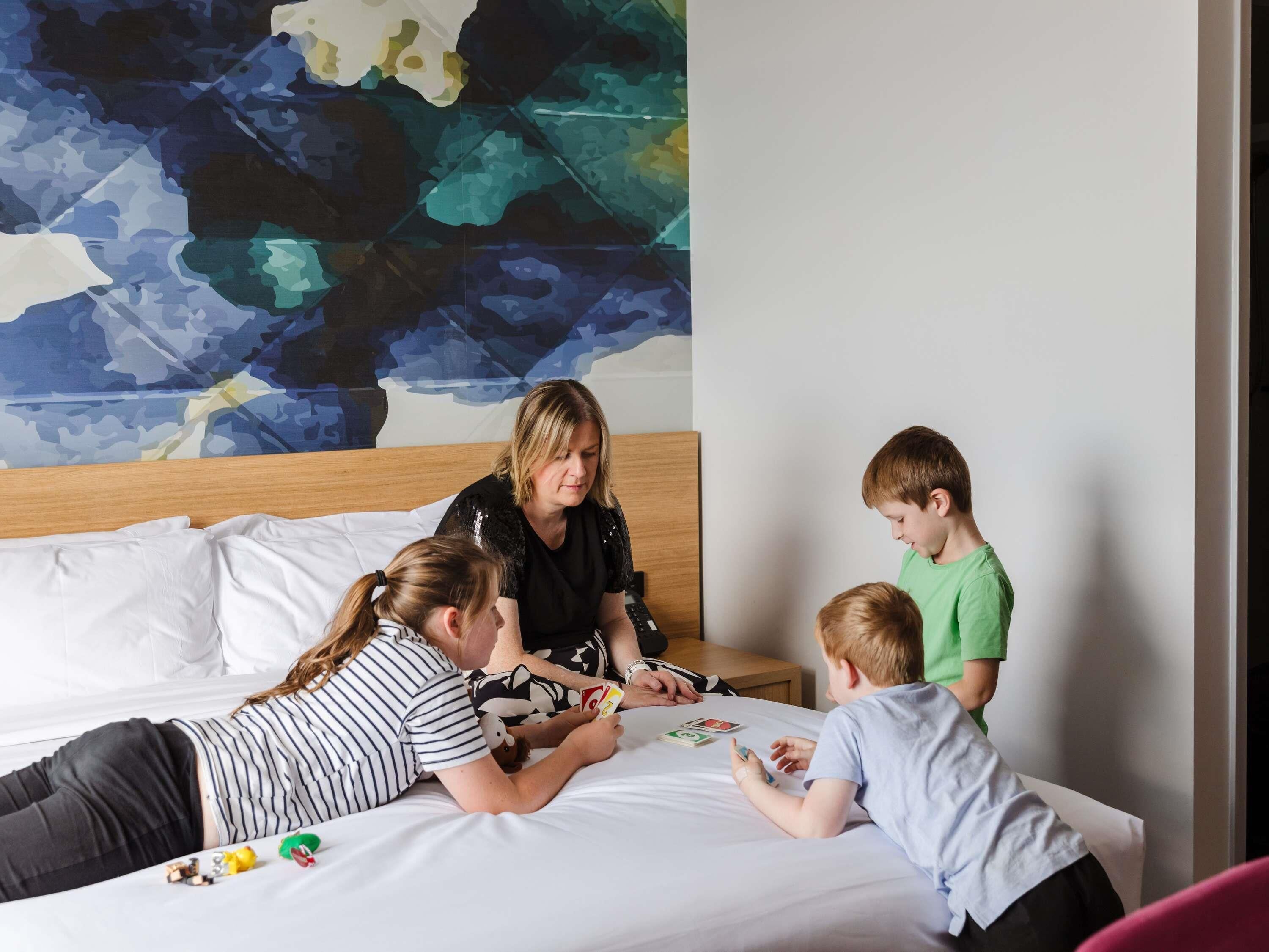 A hotel room with a bed, a wooden headboard, a large abstract painting on the wall, and a window.