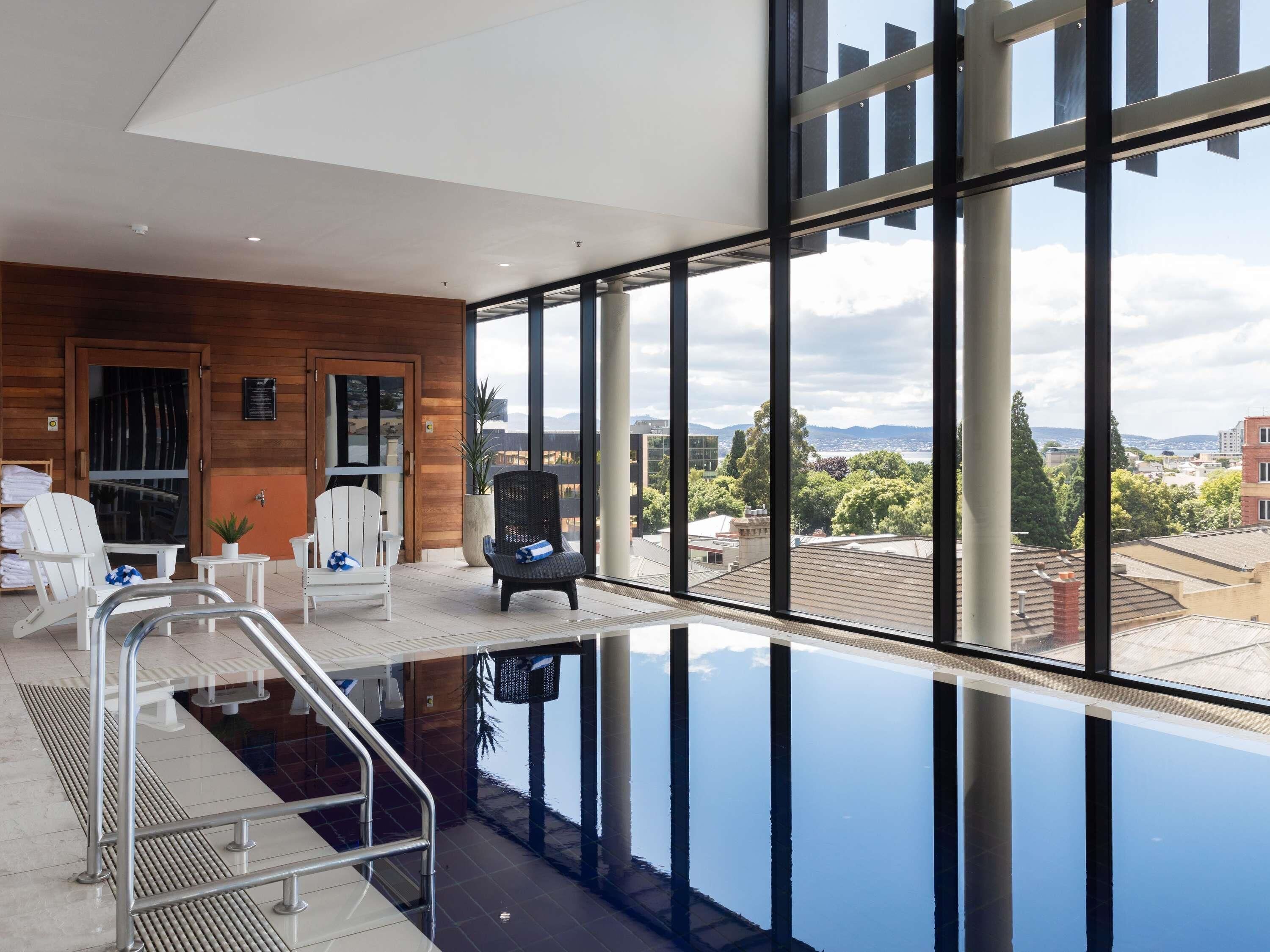 A modern indoor pool with clear views of the cityscape, a wooden wall, and seating areas.