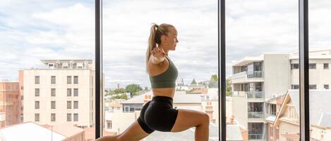 A person performing a yoga pose on a mat in a room with large windows offering a city view.