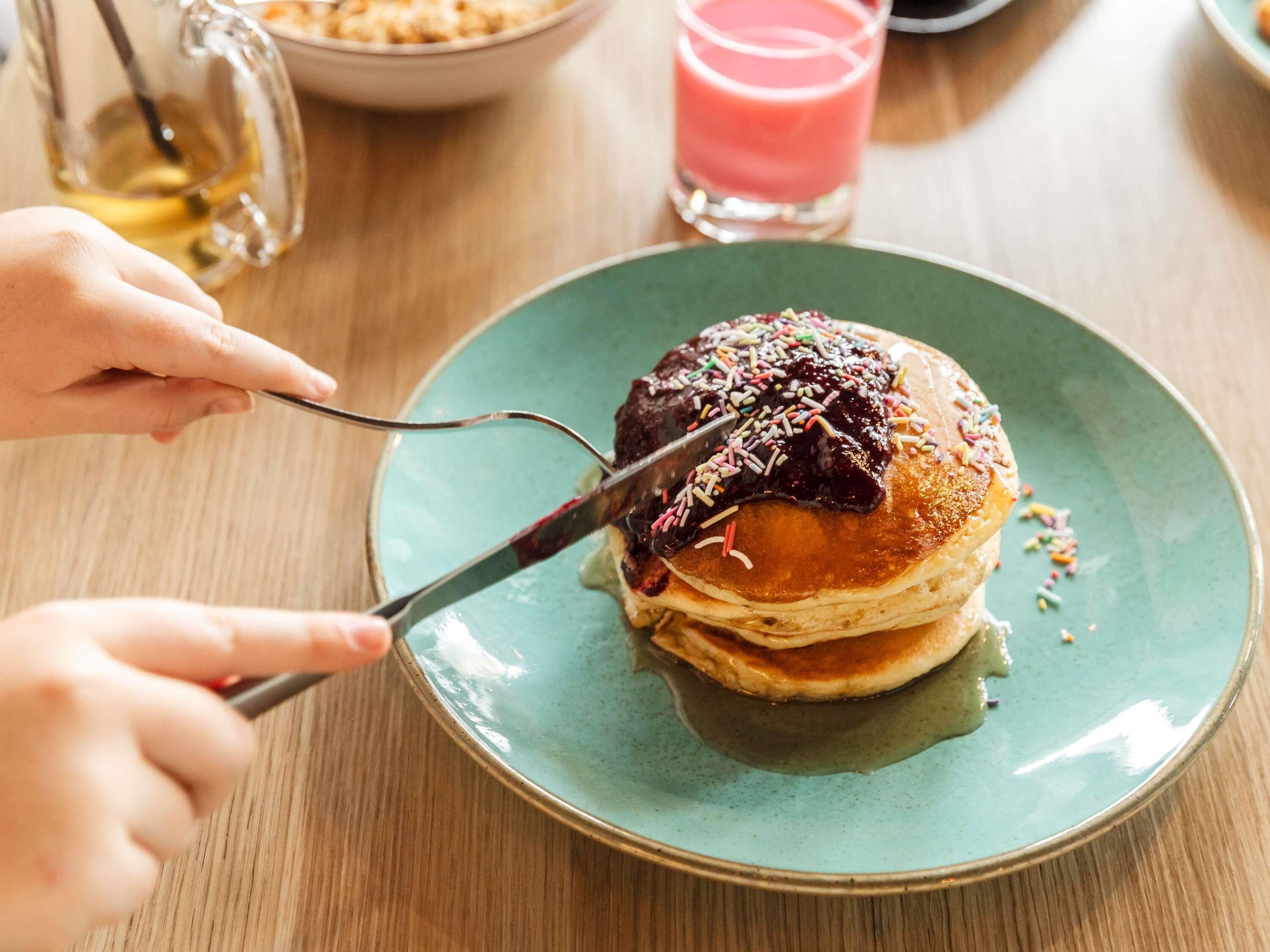 A person cutting a stack of pancakes on a green plate.