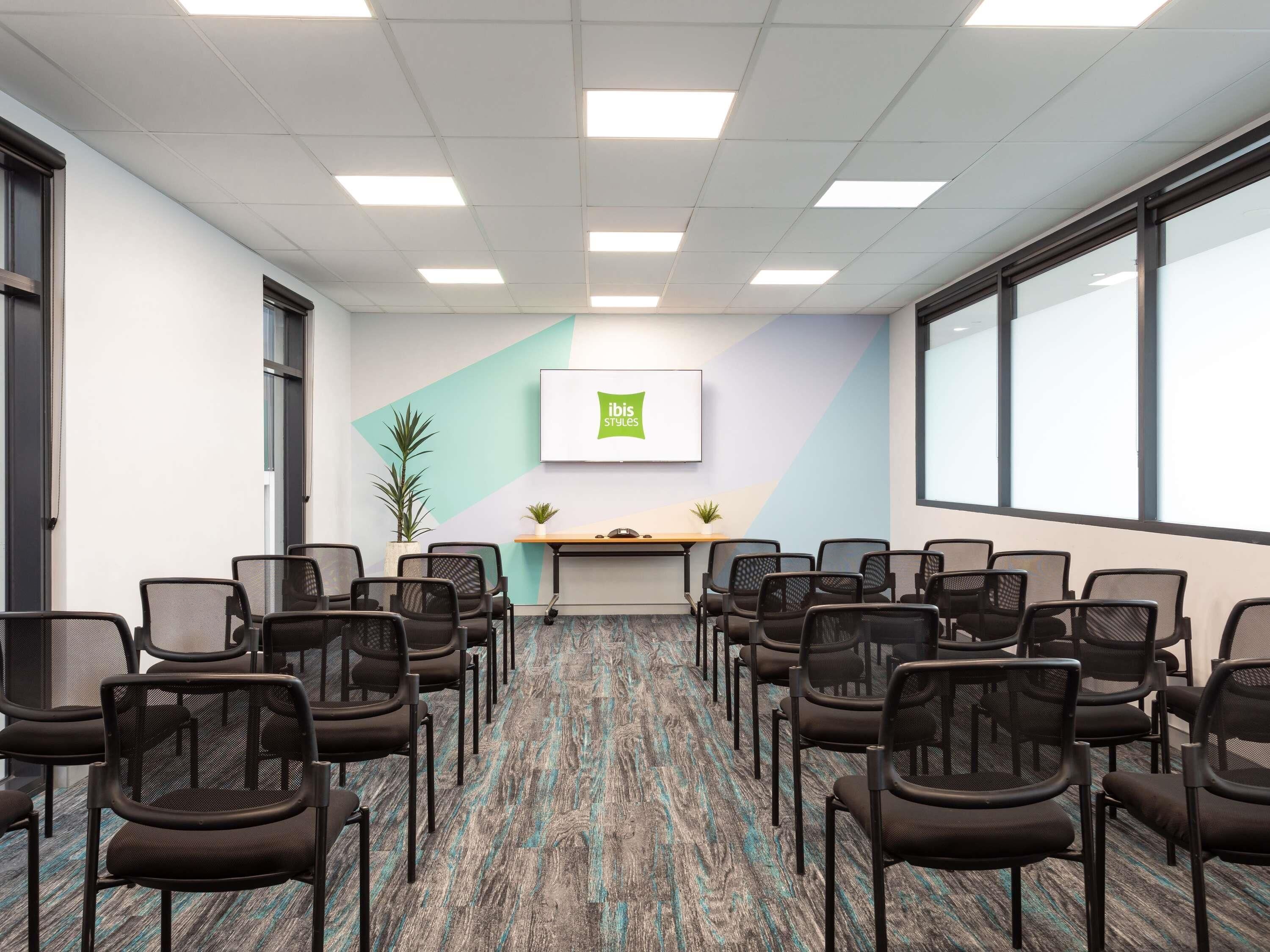 A conference room with rows of chairs, a whiteboard, and a plant on a desk.