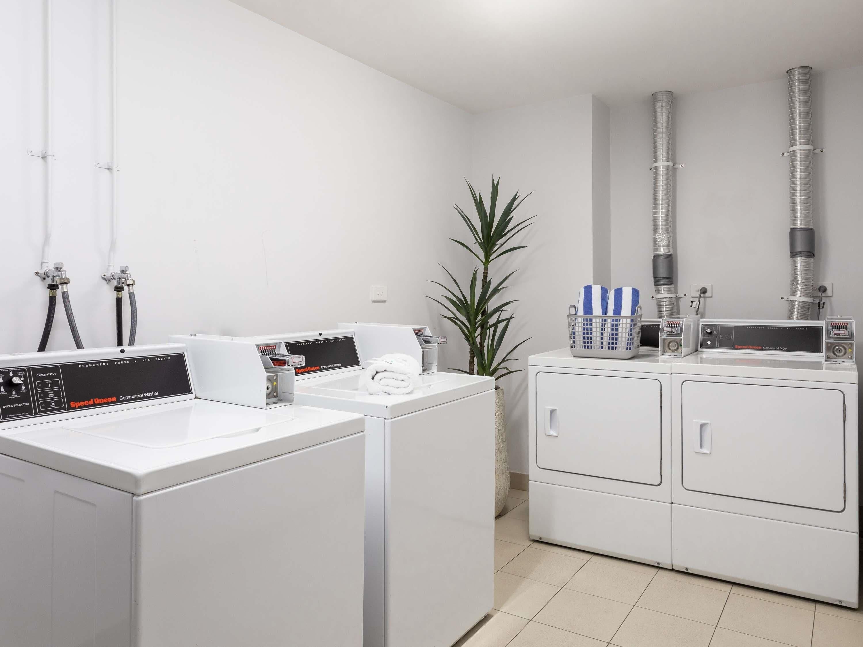 A commercial laundry facility with industrial washing machines, hoses, and a control panel.