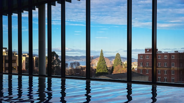 Una habitación con un ventanal grande, suelo reflectante y vistas a edificios y árboles.