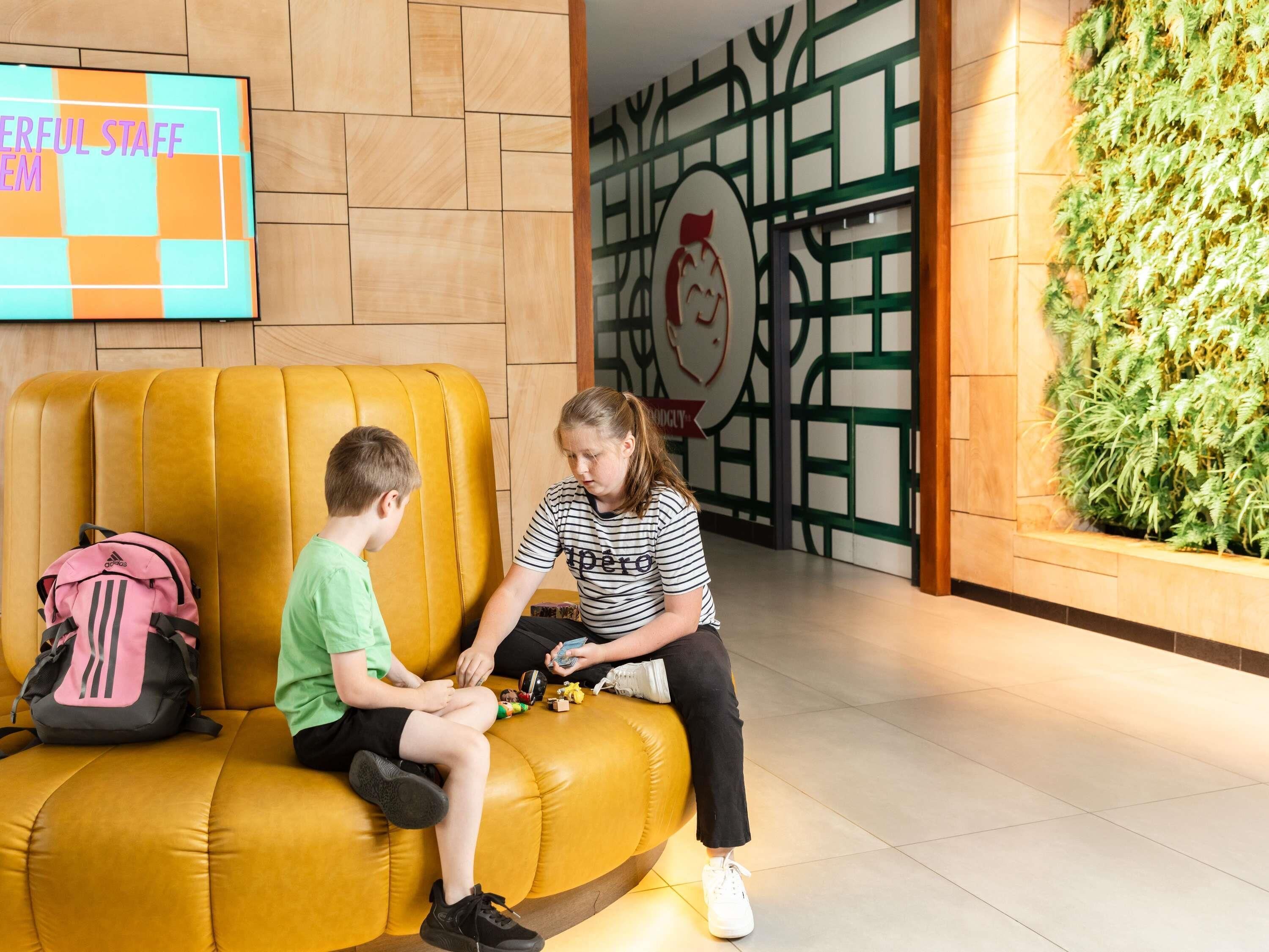 Un área de recepción con un sofá amarillo, un televisor montado en la pared y una pared verde con jardín vertical.