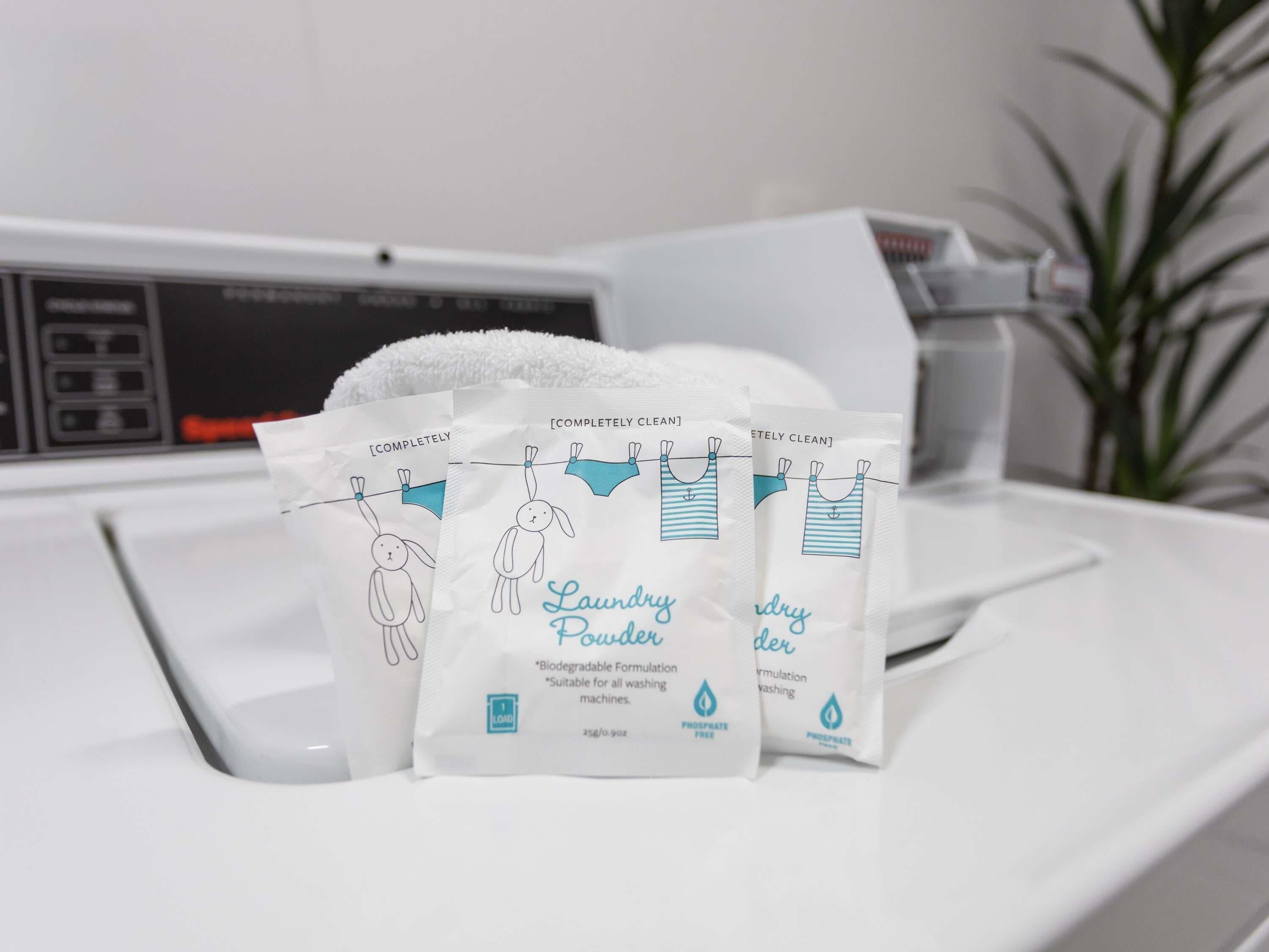 A washing machine with three laundry detergent bags labeled "Laundry Powder" on a white countertop.