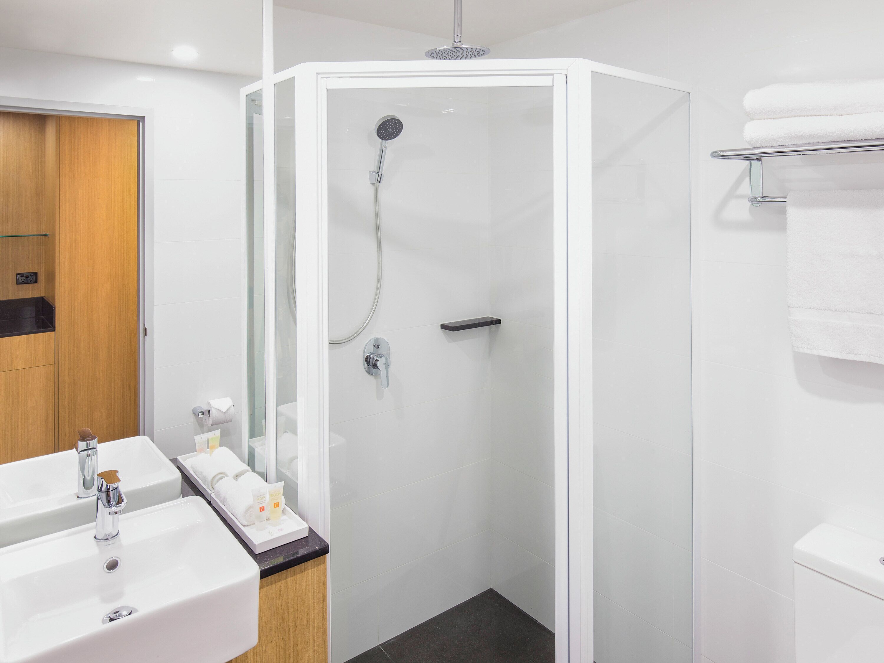 A modern bathroom with a glass-enclosed shower, a wooden vanity with a sink, and a towel rack.