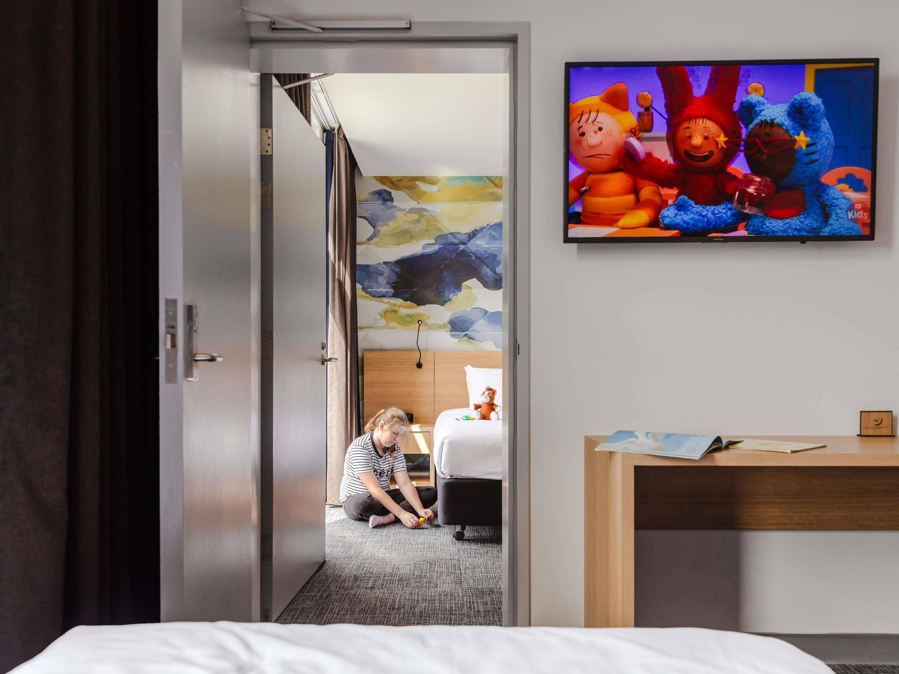 Une chambre d’hôtel avec un lit, un bureau et un téléviseur diffusant des dessins animés.
