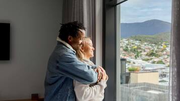 A couple embracing in a room with a large window overlooking a cityscape.