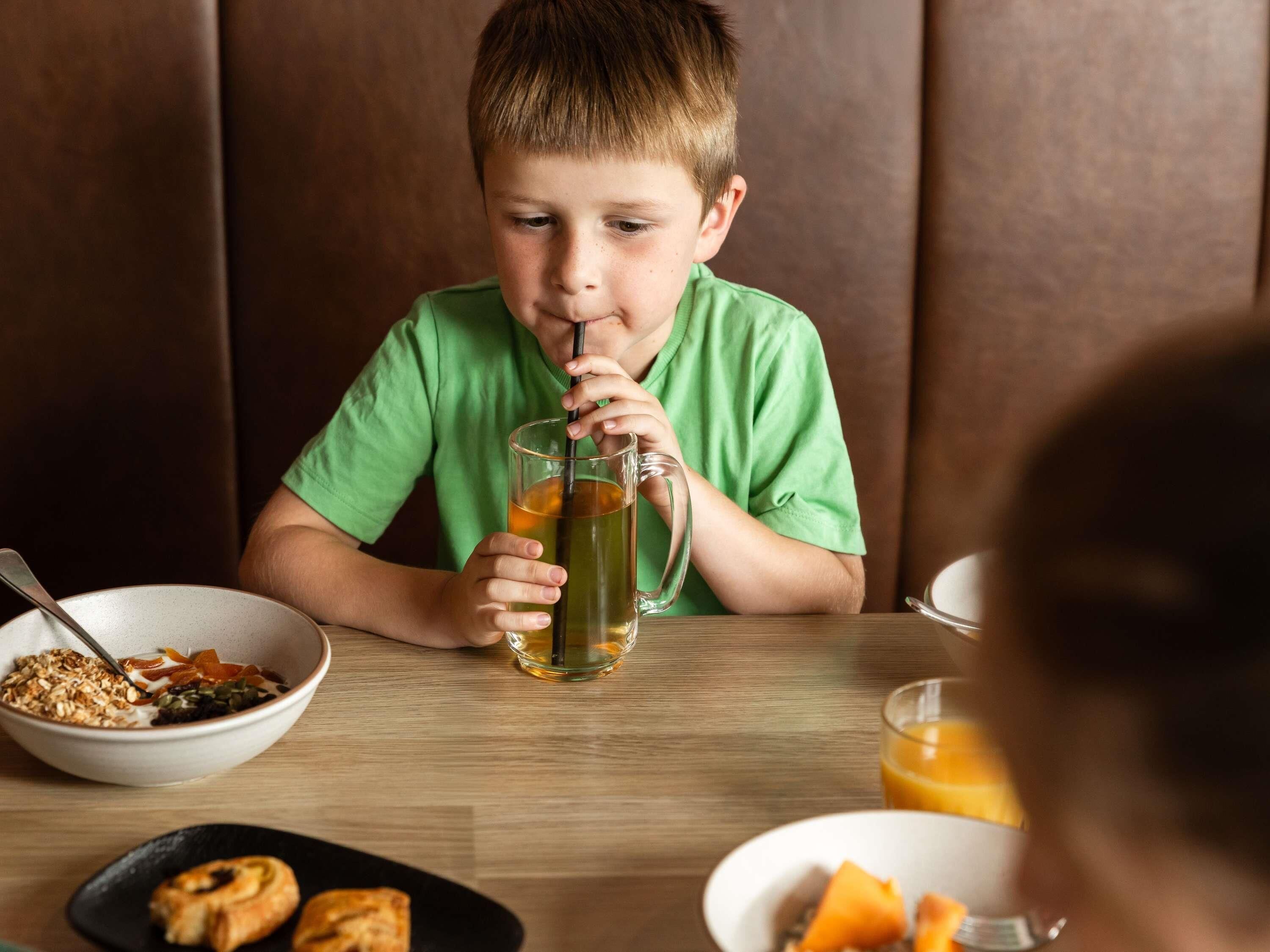 A child sitting at a table with a meal, a glass of juice, and a bowl of cereal.
