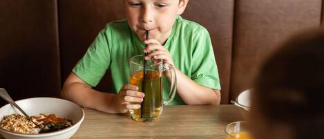 A child sitting at a table with a meal, a glass of juice, and a bowl of cereal.
