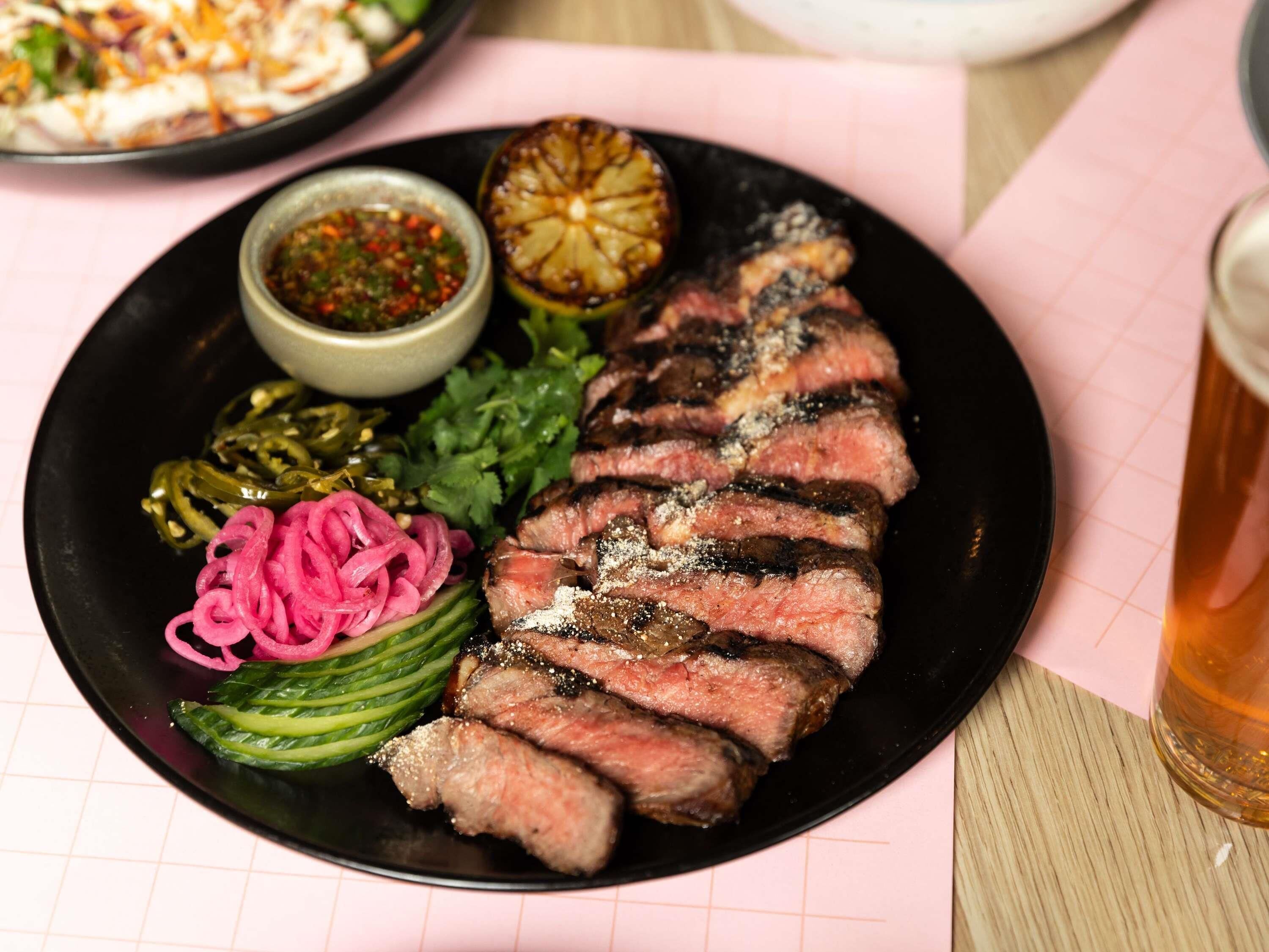 A plate with sliced steak, pickled vegetables, and a small bowl of sauce.